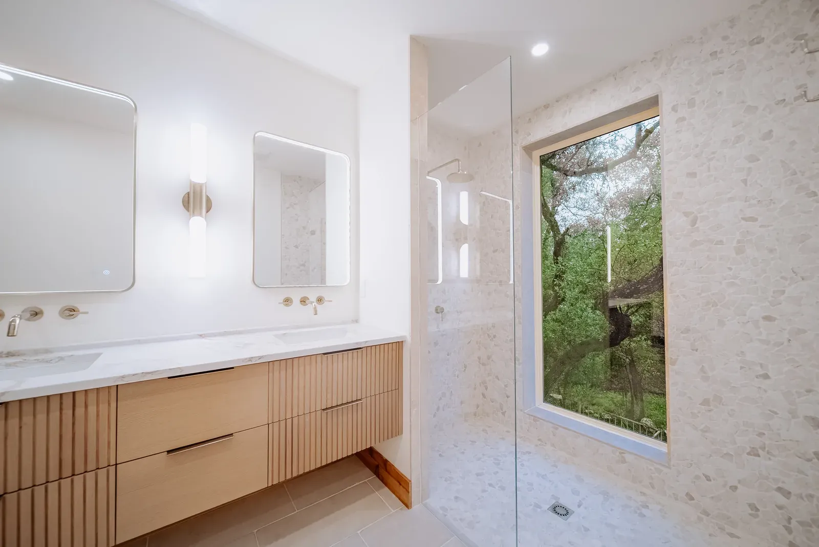 Completed Enso bathroom with pebble tile shower, white oak vanity, and a window to the trees