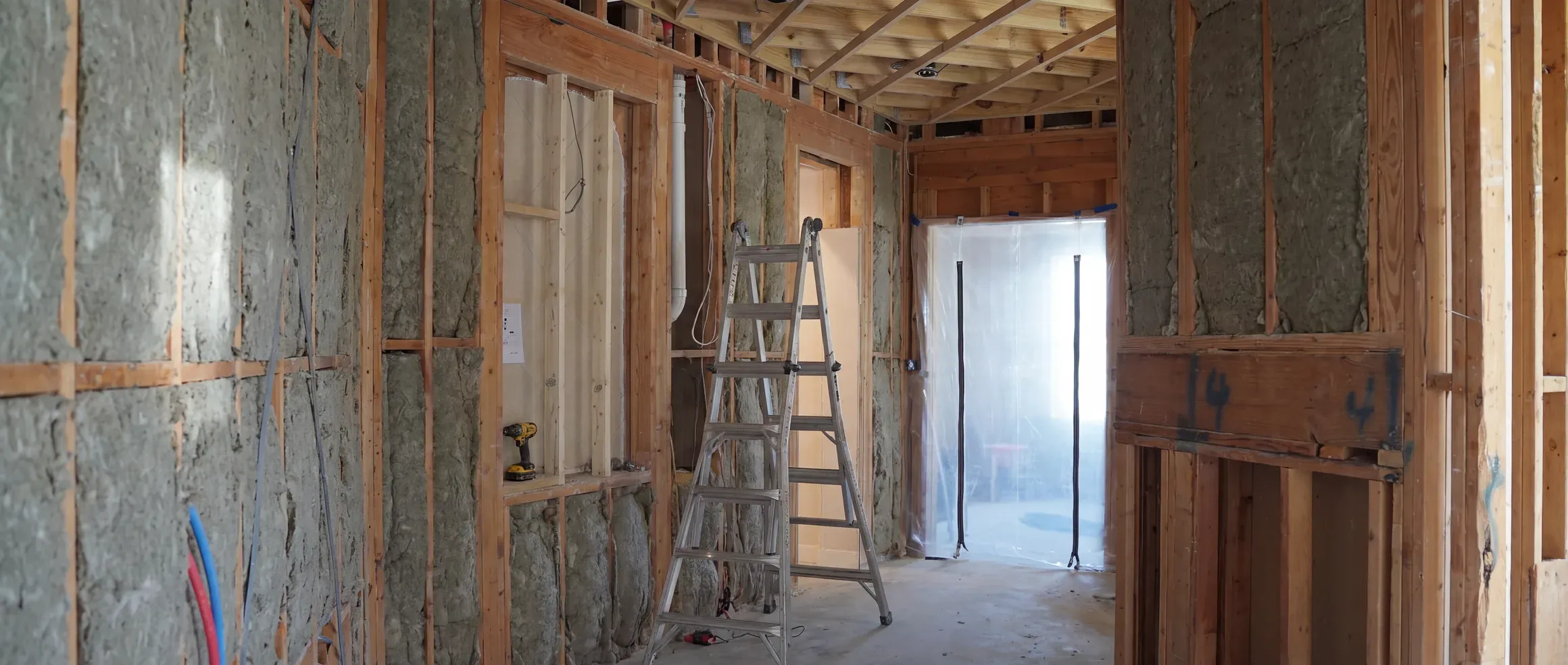 Austin whole-home remodel mid-build: an open corridor with mineral wool in every stud bay and a zip-wall barrier sealing the far end